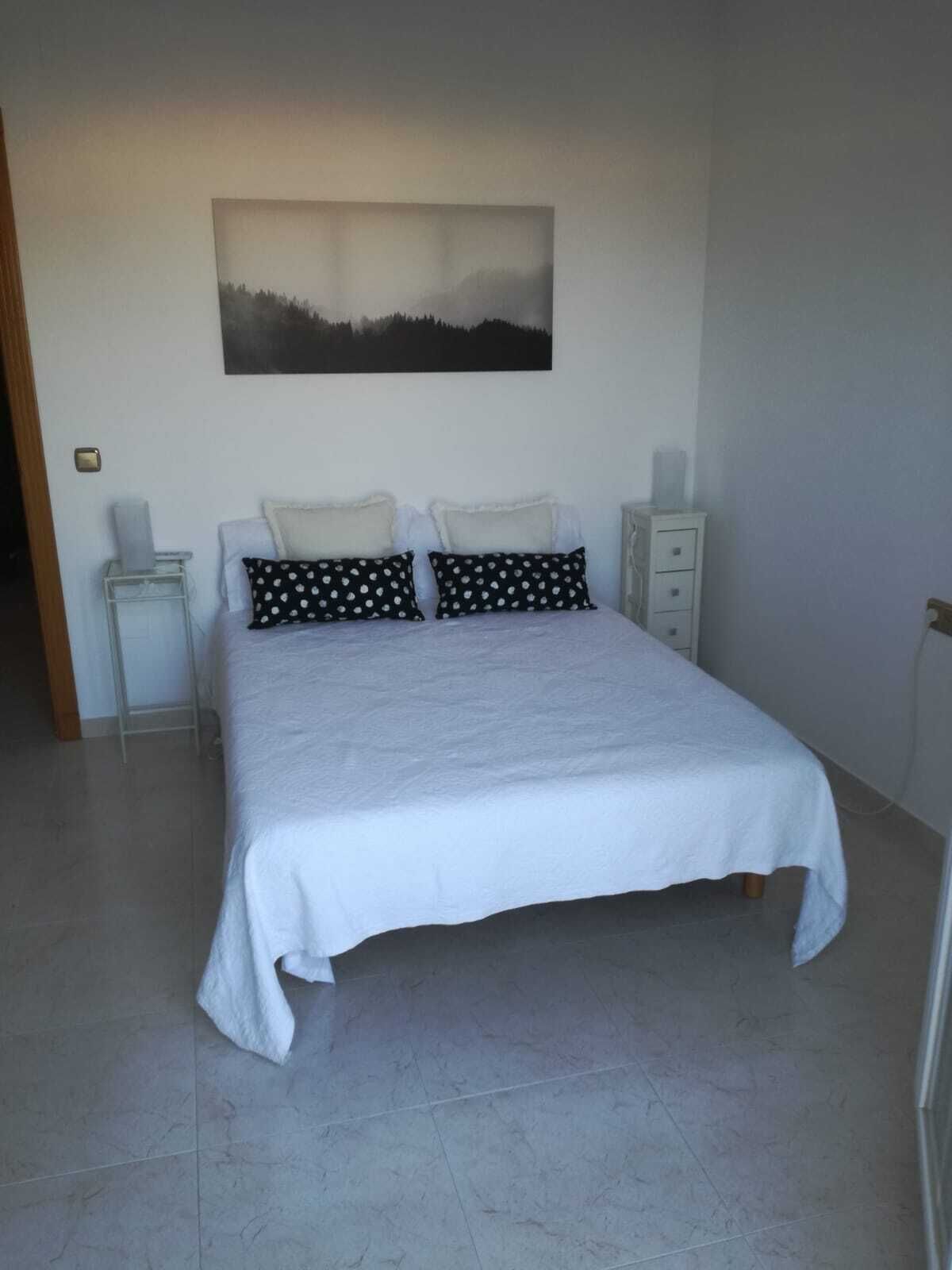 Une chambre à coucher comprenant un lit, deux tables de chevet, une commode et une lampe fixée au mur.