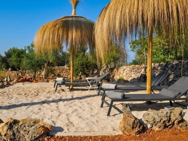 A beach with lounge chairs and thatched umbrellas.
