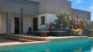 Ein modernes Haus mit Swimmingpool, Sitzgelegenheit im Freien und einem Garten mit blühenden Pflanzen.