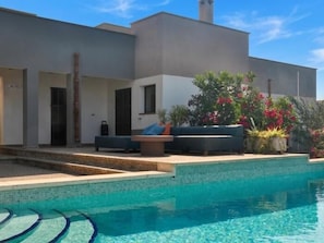 A modern house with a swimming pool, outdoor seating, and a garden with flowering plants.