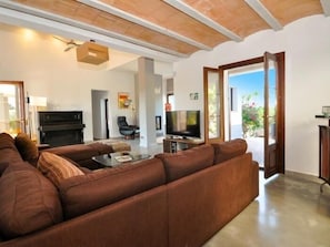 A living room with a brown sofa, a television, a piano, and a fireplace.