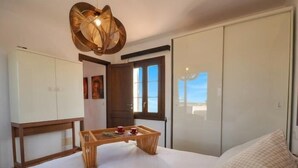 Ein Schlafzimmer mit Bett, einem Holztisch mit roter Tasse, einem Kleiderschrank und einem Fenster mit Aussicht.