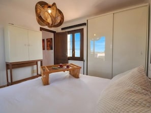 A bedroom with a bed, a wooden table with a red cup, a wardrobe, and a window with a view.