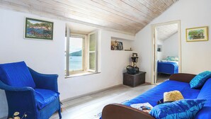 Une chambre à coucher avec un grand lit, un fauteuil bleu et une vue sur la mer par une fenêtre ouverte.
