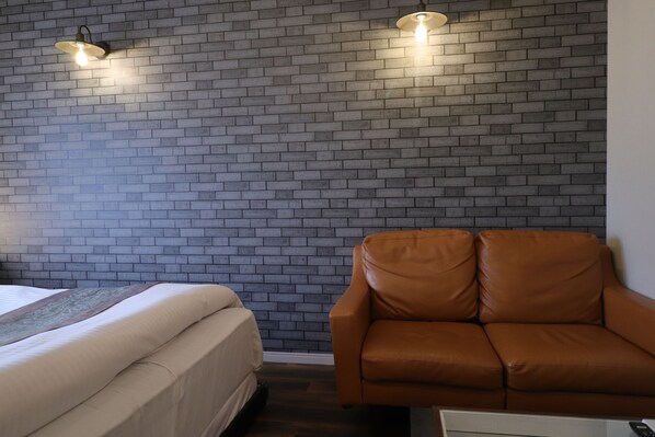 A room with a brick wall, a bed with a beige bedspread, and a brown leather sofa. - HOTEL La fontaine (Suwa)