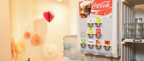 A vending machine with Coca-Cola and Aquafina water options, a water dispenser, and a shelf with glassware.