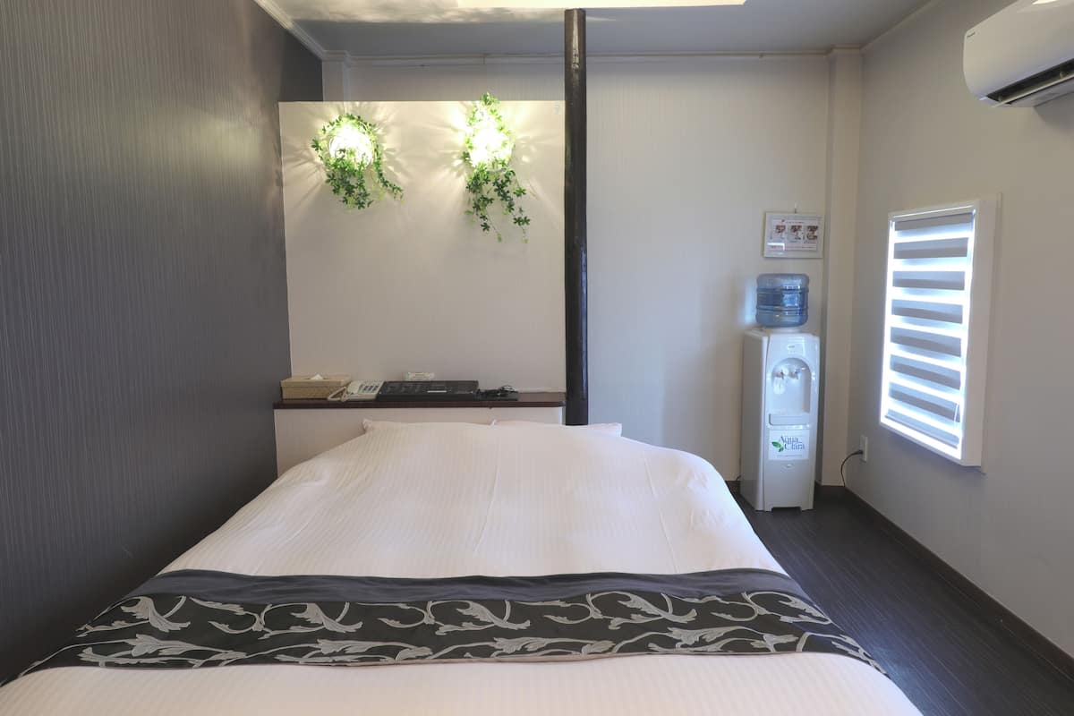 Une chambre d’hôtel avec un lit, un distributeur d’eau et une fenêtre équipée de stores.