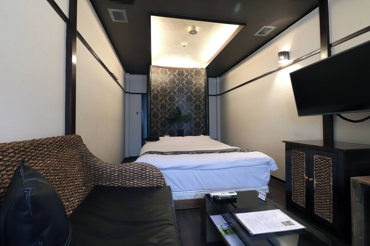 Une chambre d’hôtel compacte comprenant un lit, un canapé, un bureau avec une télécommande et un téléviseur fixé au mur.
