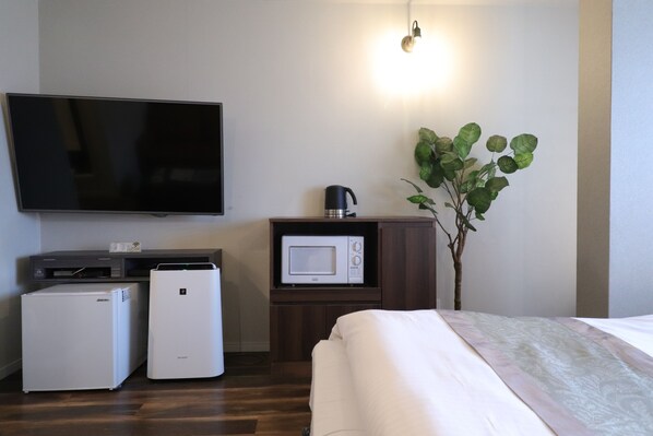 Habitación de hotel con televisión de pantalla plana, microondas, refrigerador minibar, cafetera y una planta en maceta.