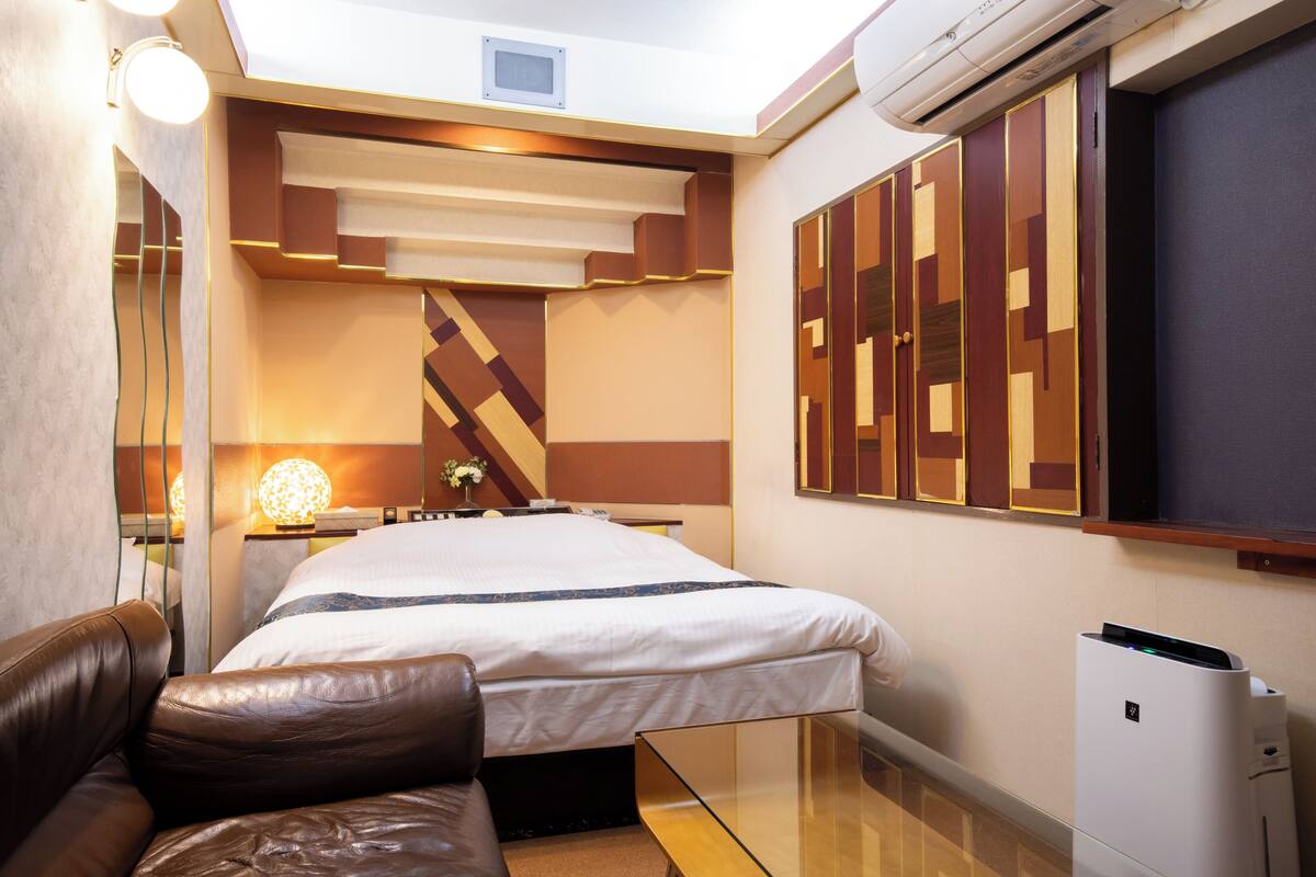 Une chambre d’hôtel moderne dotée d’un grand lit, d’un canapé en cuir, d’une table basse en verre et d’un climatiseur fixé au mur.