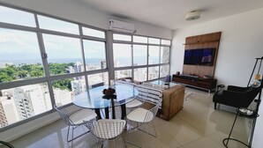 Un salon moderne avec une table en verre, des chaises blanches, un canapé et un téléviseur fixé au mur.