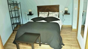 Un dormitorio con cama, mesitas de noche, un estante colgante y una pequeña mesa.