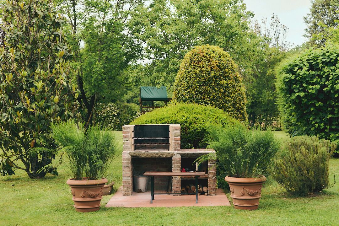 An outdoor brick barbecue area surrounded by lush greenery and potted plants.