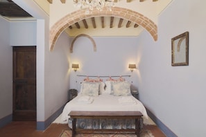 Ein Schlafzimmer mit einem Bett, zwei Wandlampen, einer Holzbank und einer gewölbten Ziegeldecke.