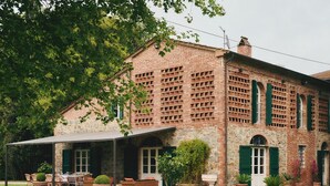 Ein Backsteinhaus mit überdachter Terrasse, Sitzgelegenheiten im Freien und Kübelpflanzen.
