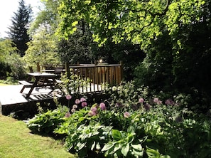 Eine Garten-Terrasse mit Holzdeck, umgeben von üppiger Vegetation und blühenden Pflanzen.