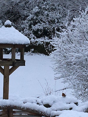Ein hölzerner Pavillon, bedeckt mit Schnee, umgeben von schneebedeckten Bäumen und Sträuchern.