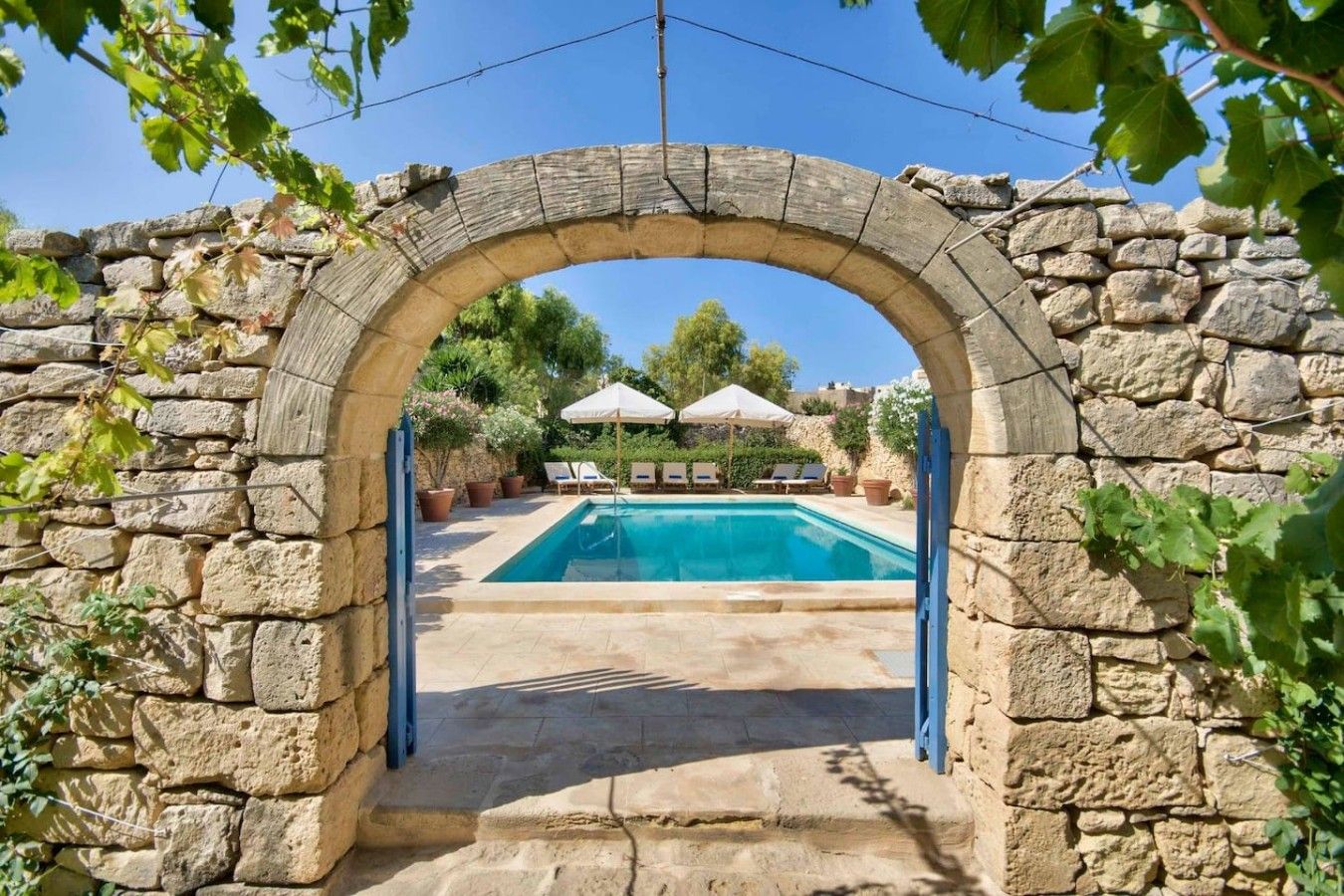 Un arc en pierre mène à un espace piscine agrémenté de chaises longues et de parasols.