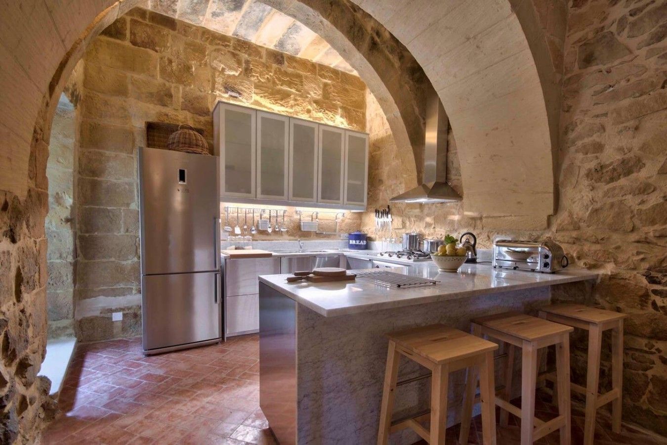 A kitchen with stone walls, a central island, bar stools, and modern appliances.