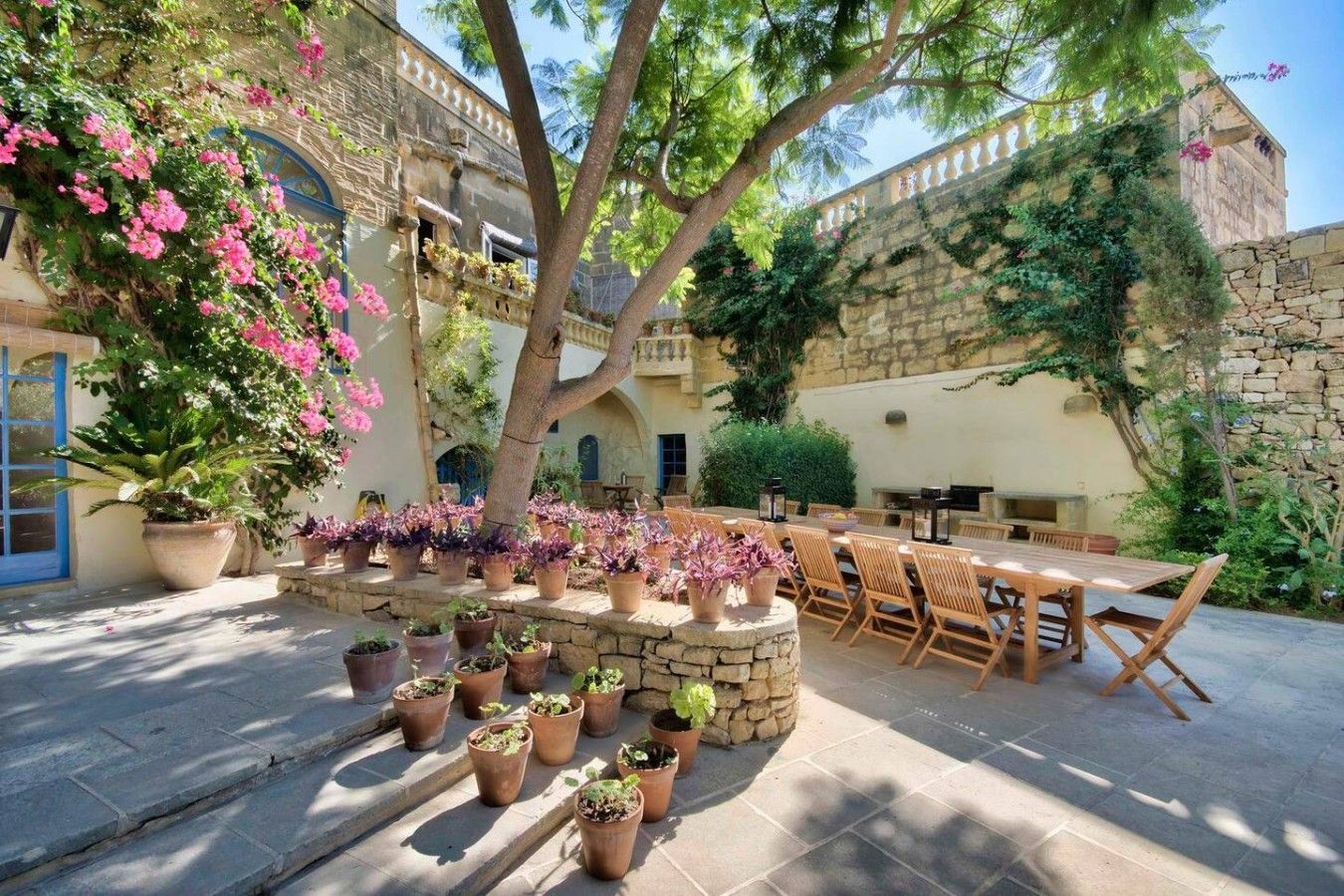 An outdoor dining area with stone walls, potted plants, and a wooden table and chairs.