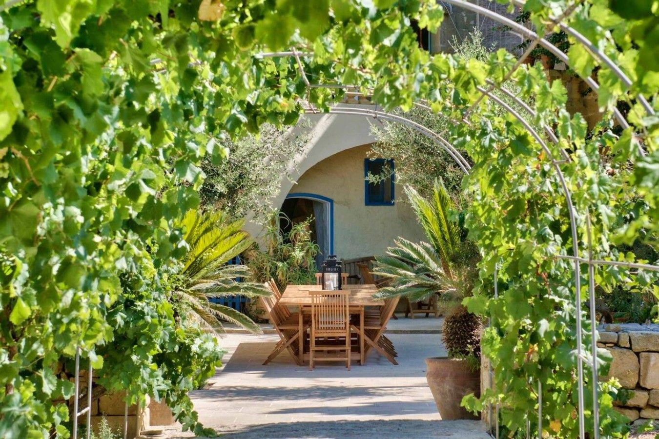 A patio with a table and chairs, surrounded by greenery and a stone wall.