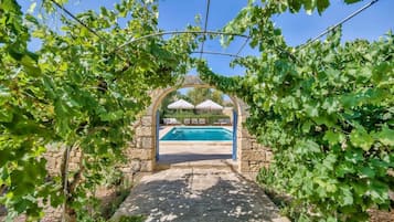 A stone archway leading to a swimming pool surrounded by lush greenery.