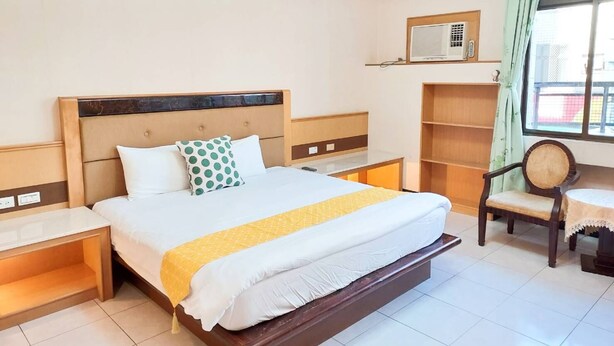 A hotel room with a large bed, bedside tables, a chair, a window with curtains, and a built-in shelf. - Ancient City Hostel (Hengchun)