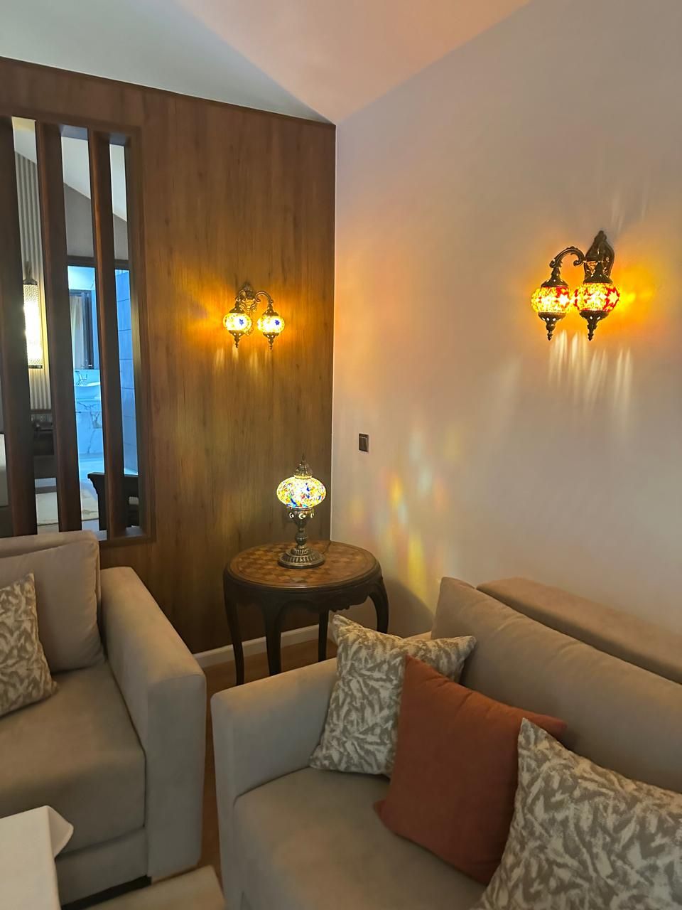 Een woonkamer met een bank, een klein rond tafeltje met een lamp, en twee wandlampen.