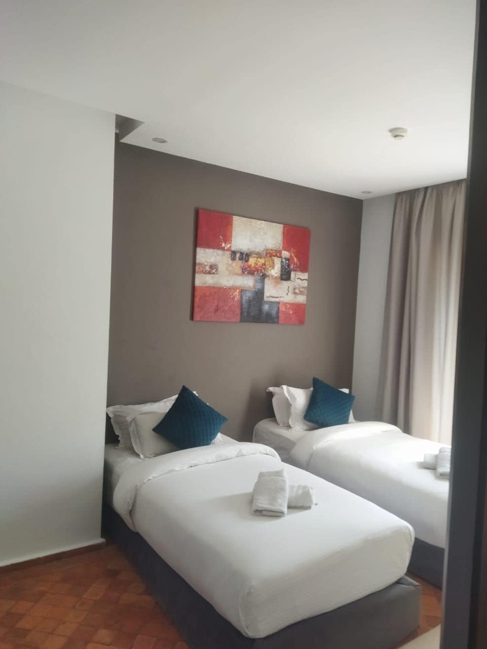 A hotel room with two beds, a painting on the wall, and a window with curtains.