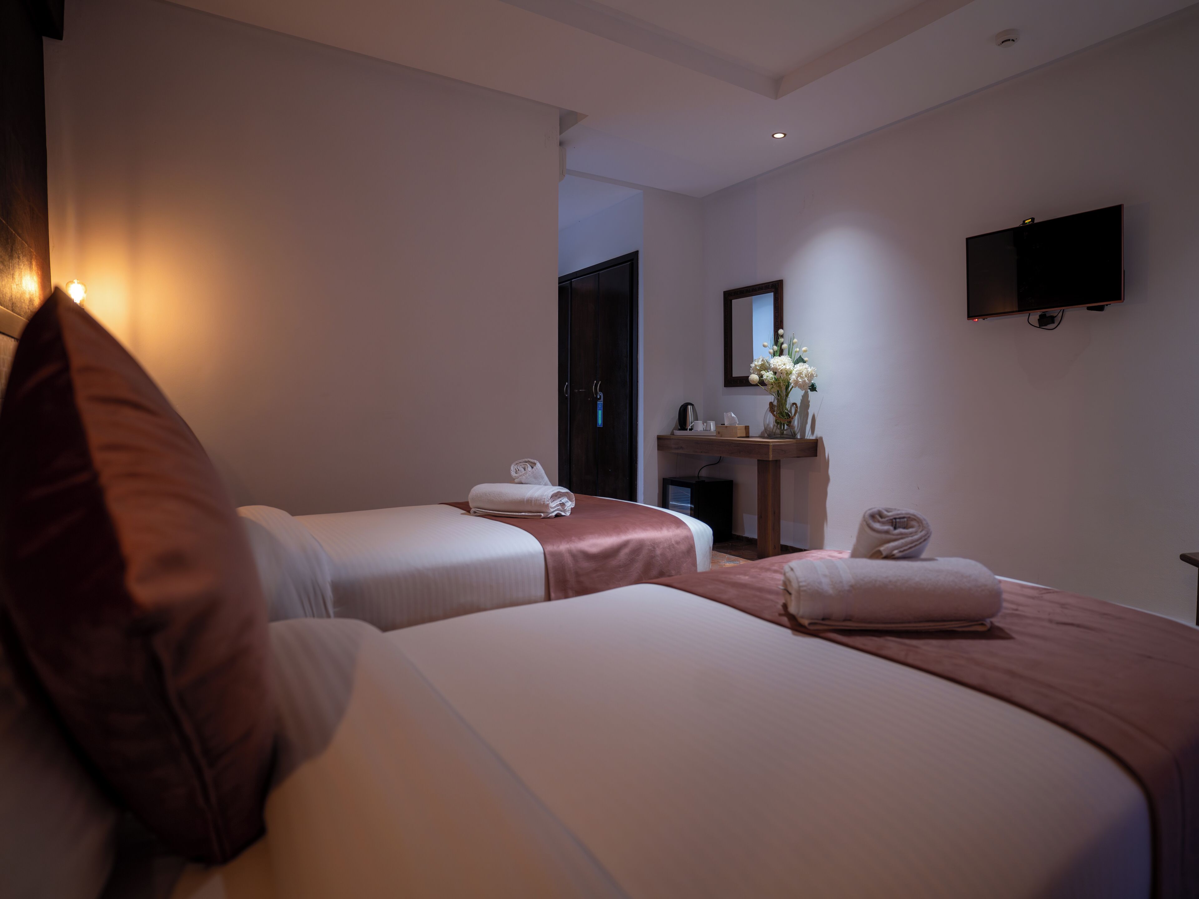 Ein Hotelzimmer mit zwei Betten, einem Schreibtisch mit Spiegel, einem Flachbildfernseher und einem kleinen Schrank.