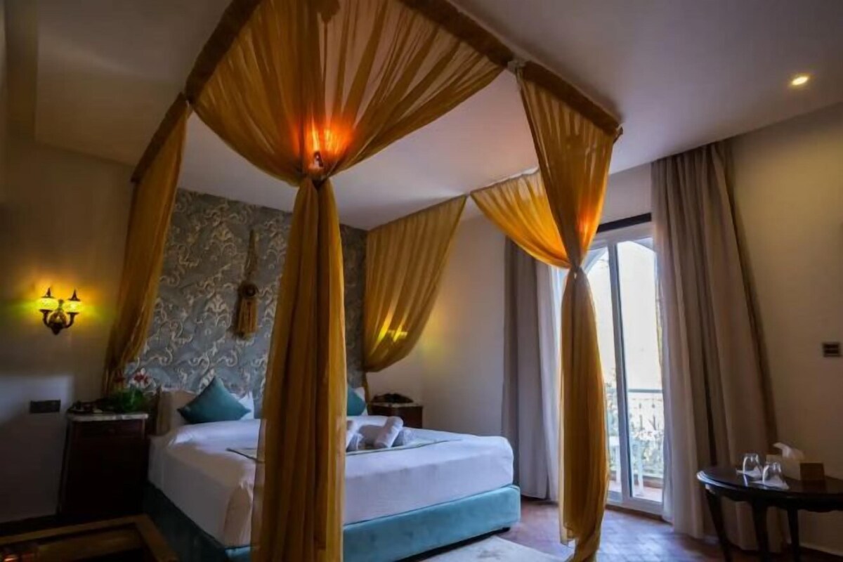 A bedroom with a four-poster bed, a nightstand, a bedside table, and a view of the outside balcony.