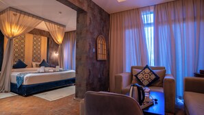 A hotel room with a bed, a sofa, a coffee table, and a window with curtains. - Dar Ba Sidi & Spa (Derdara)