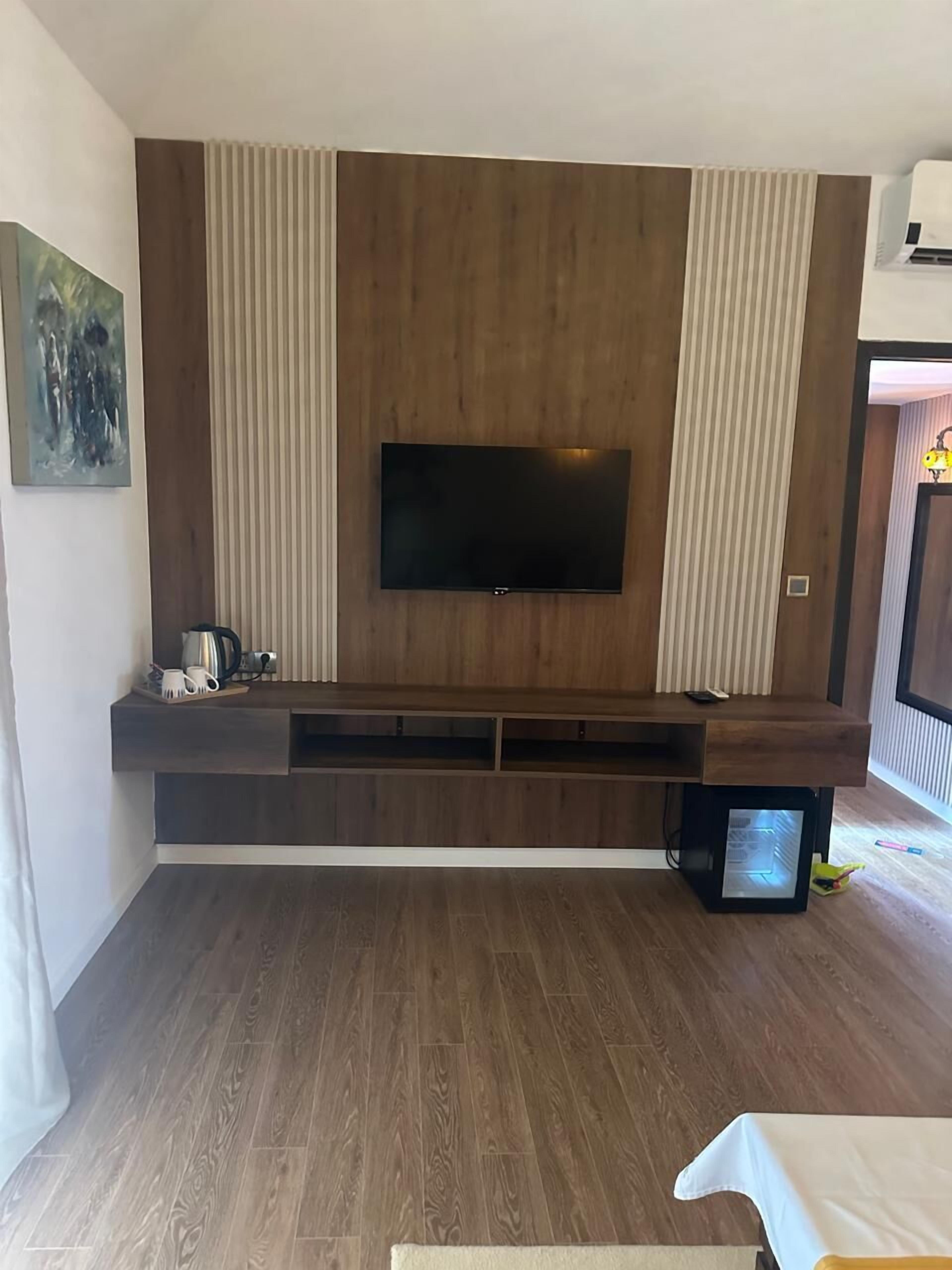 A modern living room with a flat-screen TV mounted on a wooden wall, a built-in entertainment unit, and a wooden floor.
