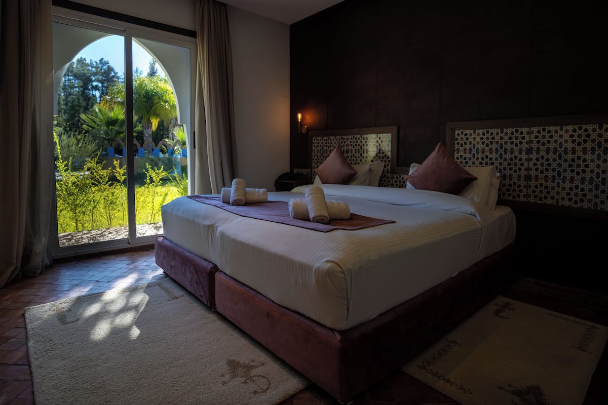 A spacious bedroom with a large bed, a view of greenery through a sliding door, and a patterned headboard.