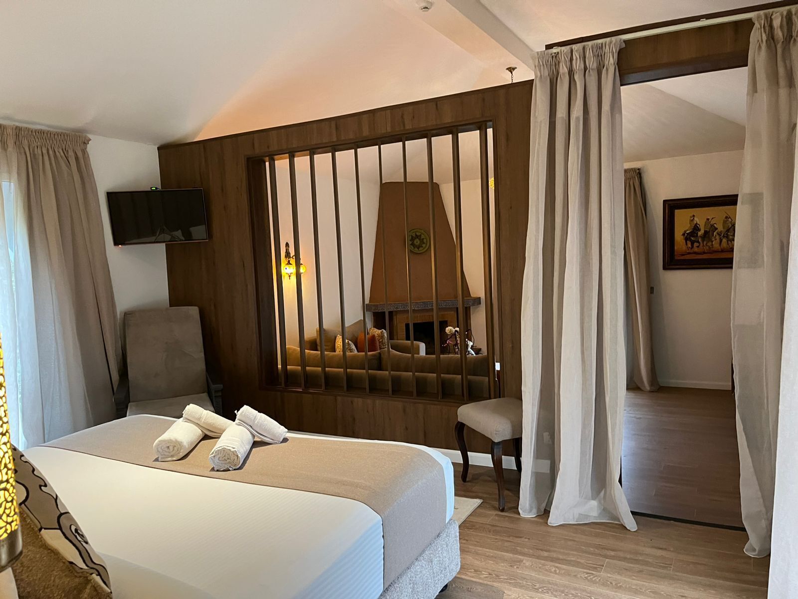 Een hotelkamer met een bed, een stoel, een open haard, een televisie en een schilderij aan de muur.