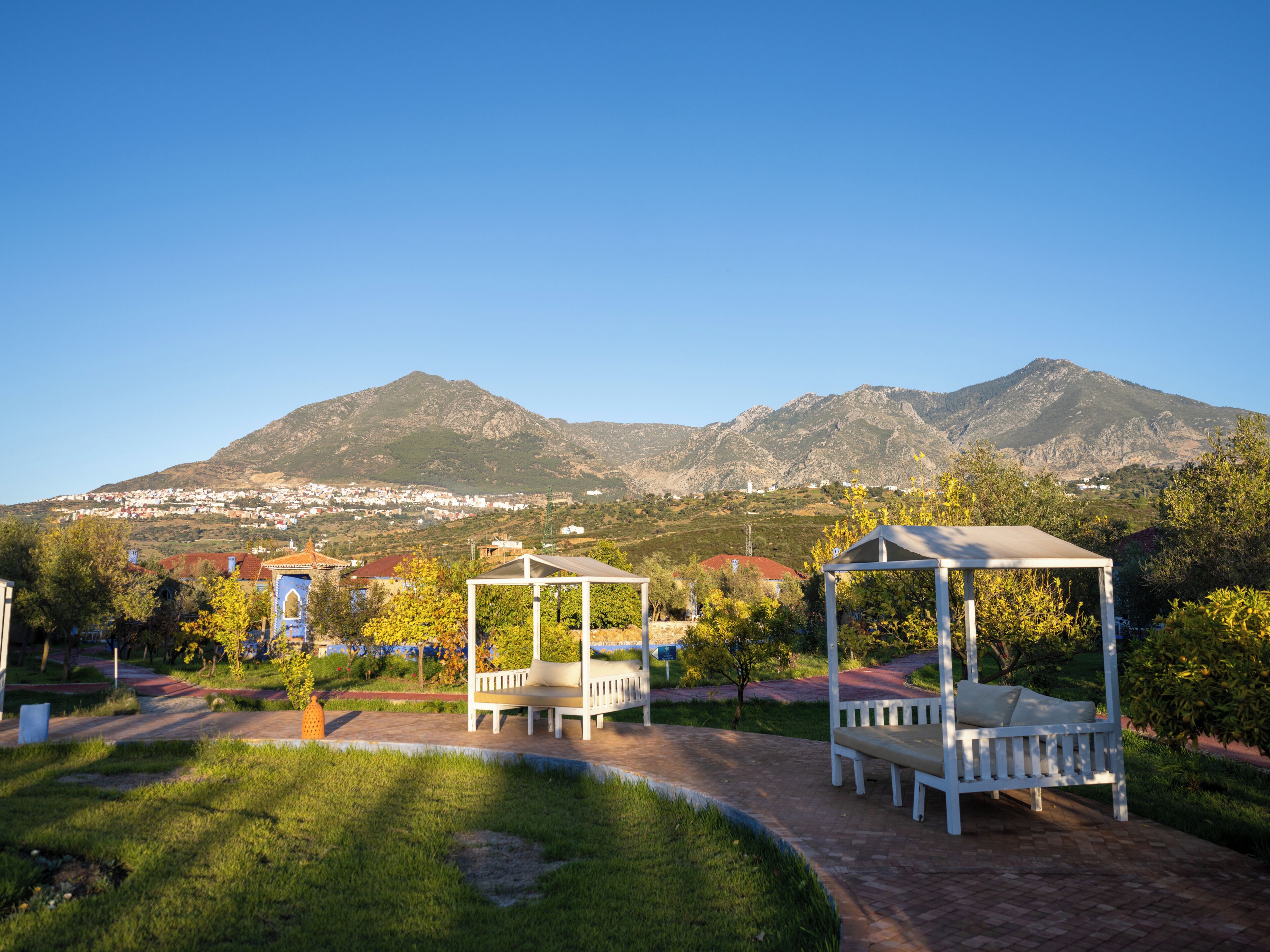 A park with white gazebos and benches, a paved walkway, and a mountain backdrop.