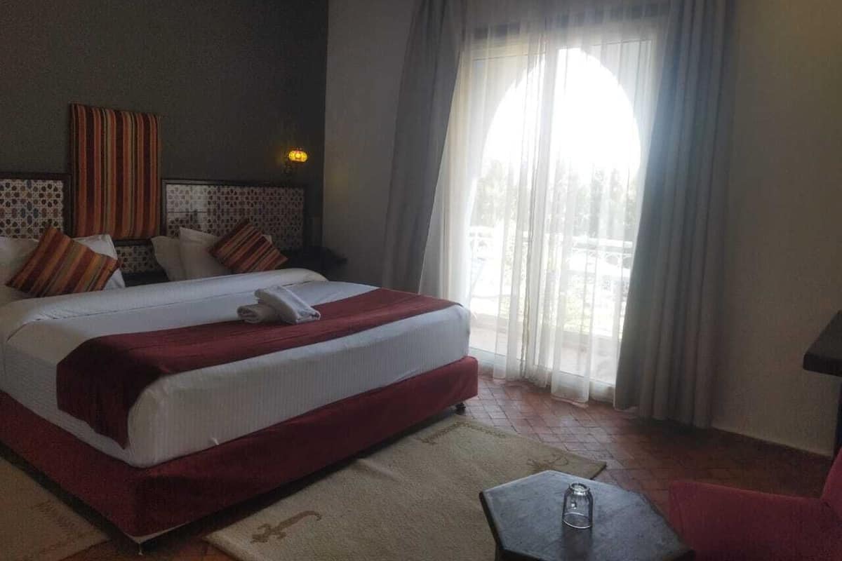 A hotel room with a large bed, a small table, and a view of the outdoors.