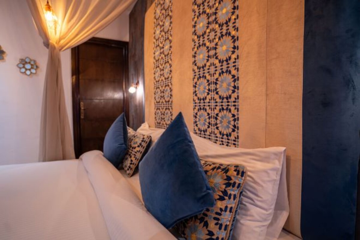 A neatly made bed with blue and white pillows, a dark wooden door, and patterned wall decor.