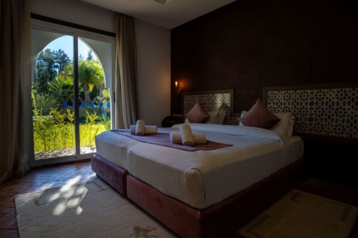 A large bed with a headboard, a view of greenery through a glass door, and a patterned wall.