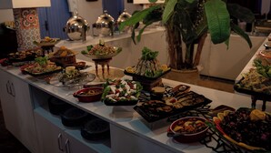 A buffet with various dishes, a clock on the wall, and a large plant. - Dar Ba Sidi & Spa (Derdara)