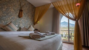 A hotel room with a bed, pillows, a window with curtains, a balcony, and a view of mountains. - Dar Ba Sidi & Spa (Derdara)