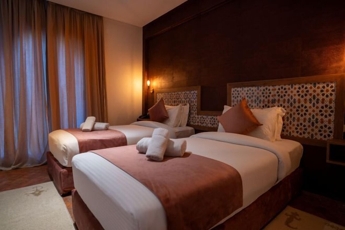 Una habitación de hotel con dos camas, cada una con cabecera, mesita de noche y lámpara.