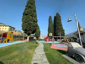 Explore the playground with a slide and climbing structure, surrounded by tall trees and traditional buildings.