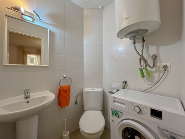 Un baño con lavamanos, inodoro y lavadora.
