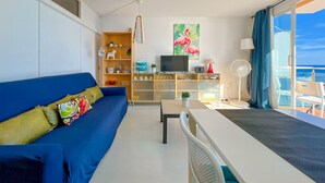 Una sala de estar moderna con un sofá azul, un televisor y una zona de comedor con mesa y sillas.
