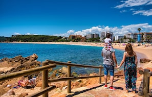 Una spiaggia con costa rocciosa, ringhiere in legno e edifici sullo sfondo.
