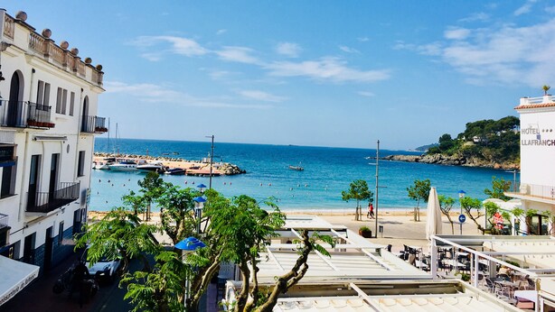 A coastal hotel with outdoor seating overlooking the sea, a beach, and rocky terrain.