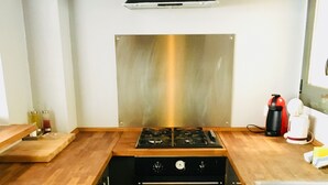 A compact kitchen with a stainless steel range hood, a gas stove, and a built-in oven. There is a wooden countertop and a stainless steel sink.