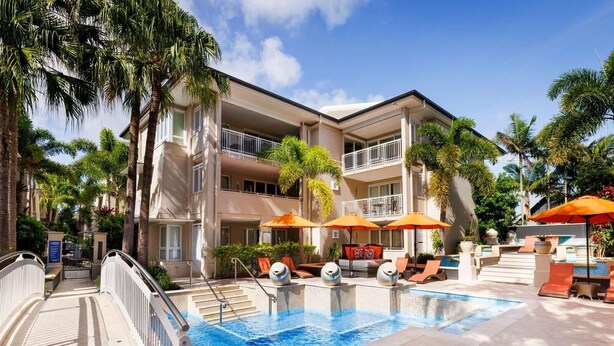 Un hôtel doté d’une piscine, d’un espace extérieur aménagé et de palmiers.