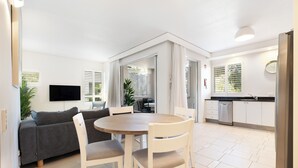 Une cuisine moderne avec des meubles blancs, un réfrigérateur en acier inoxydable et un coin repas comprenant une table ronde et des chaises blanches.